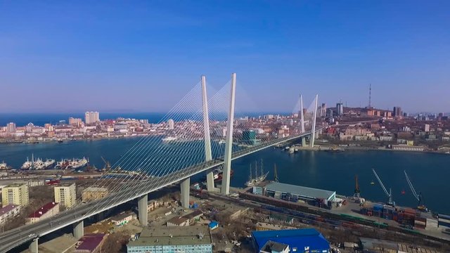 Zolotoy Rog Bay. Bridge Near Vladivostok. Industrial Buildings in Port. Cranes Working. City Hills on Coast. Ships in Dock. Autumn. Wide Shot. Aerial