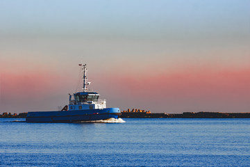 Fototapeta premium Blue small tug ship sailing past the breakwater dam in morning