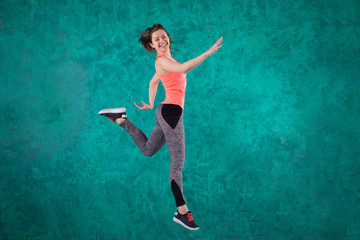 Sport young female  in fashion sportswear jumping over turquoise background.