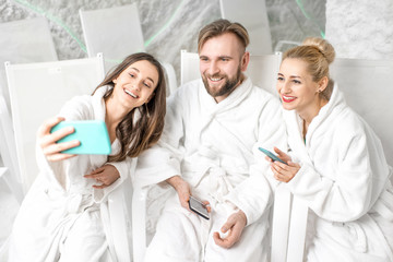 Obraz premium Three friends in bathrobes making selfie photo together with phone in the salt room