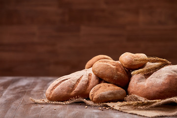 handmade tasty bread lying on burlap on the wooden table with flour, wheat and ears of wheat. Brown blurred background.