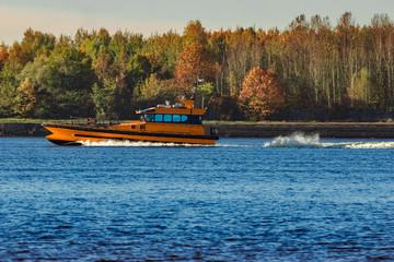 Fototapeta premium Orange pilot ship sailing past the autumn trees in Europe
