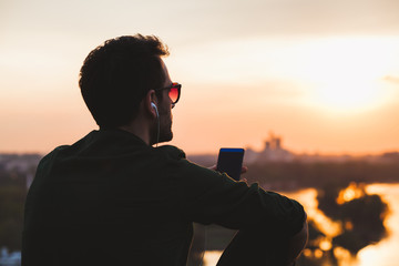 Young man enjoying sunset listening to the music on the smartphone
