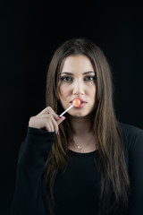 Young woman touching a lollipop on her juicy big lips, wear a black blouse,isolated black background