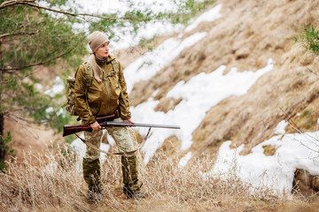 woman hunter in camouflage clothes ready to hunt, holding gun and walking in forest. hunting and people concept