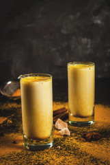 Traditional Indian drink turmeric milk is golden milk with cinnamon, cloves, pepper and turmeric. On a concrete table, with spices on the background. In glasses, toned copy space