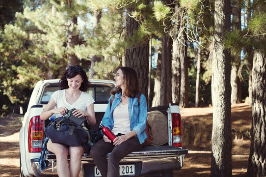 Happy female friends talking while sitting on pick-up truck in forest