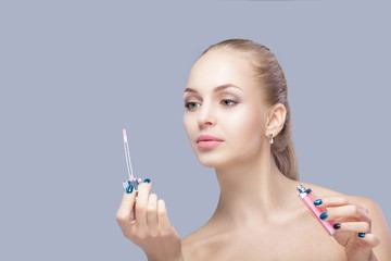 Obraz premium beautiful blond woman holding pink lip gloss on gray background. lip makeup