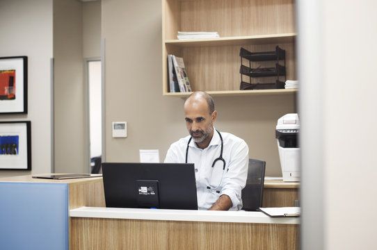 Doctor using desktop computer while working in room at hospital seen through glass