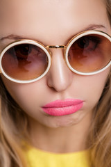 portrait of unhappy and frustrated blond woman in sunglasses and yellow shirt on blue background.  