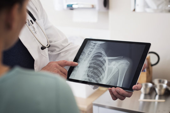 Midsection Of Doctor Showing X-ray Image On Tablet Computer To Patient In Hospital