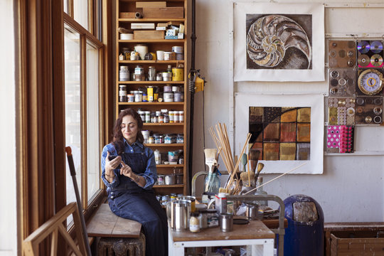 Female artist using smartphone while sitting on table at workshop