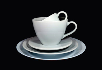 Piled up white porcelain tea cups and coffee cups with saucers in different size on black background 