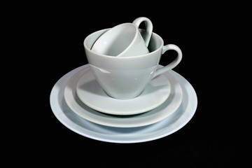 Pile of two white porcelain tea cup with saucers and plate isolated on black background, minimalist image 