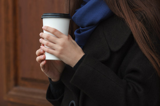 Young woman hands with coffee disposable cup outdoors with wooden doors background