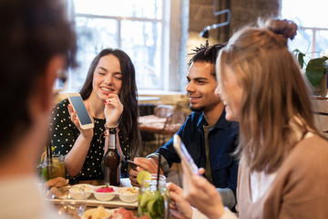 friends with smartphones and food at bar or cafe