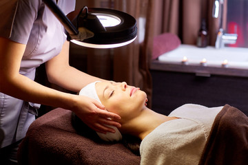 beautician doing face massage to woman at spa