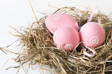 Easter concept. Nest of hay with painted pink eggs on a white background. Close up.
