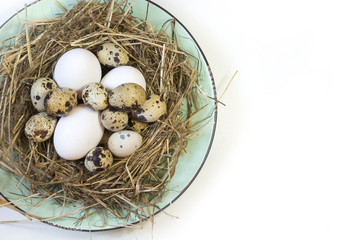 Naklejka na ściany i meble Easter concept. Nest of hay with white chicken and quail eggs in plate on a white background. Top view and copy space.