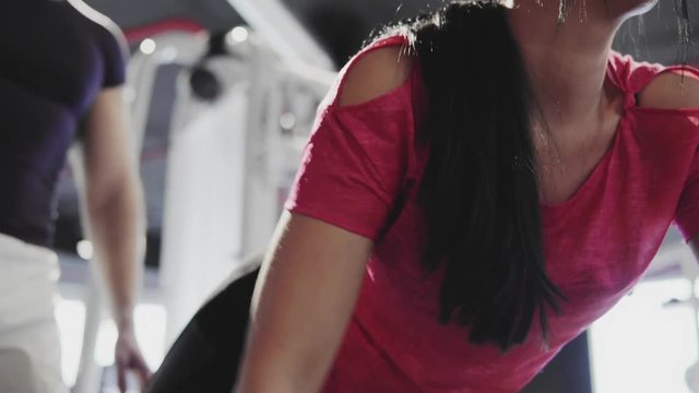 A young woman is engaged in a gym with a personal trainer. The fitness coach explains and shows the technique of doing the exercises. 4K