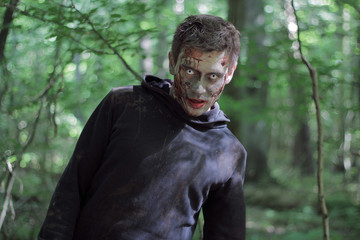 Zombie in a jacket with a hood in a forest.