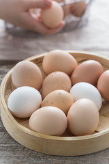 Farm fresh eggs in a bamboo basket. Female hands and more eggs in the background. 