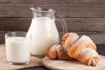 jug and glass of milk with croissants on a wooden background