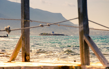 Obraz premium Typical summer image of an amazing pictorial view through a frame of a wooden pier and ropes of an old white church in a small island, Malia, Crete, Greece.