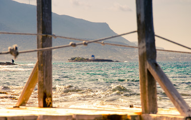 Typical summer image of an amazing pictorial view through a frame of a wooden pier and ropes of an old white church in a small island, Malia, Crete, Greece.