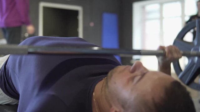A young sporty man raises the barbell lying down. 4K