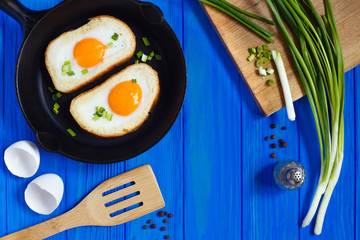 Fried eggs in toast with spices and spring onion on blue wooden background.