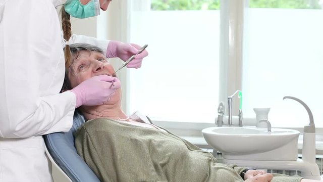 Elderly woman showing aching tooth to female dentist while sitting in dental chair 