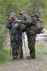 Two men in camouflage uniforms and backpacks to define your way across the map using a compass.