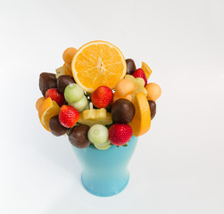 beautiful closeup view of assorted various natural appetizing fruits mixed with dark chocolate bouquet in ceramic blue vase on white grayish background