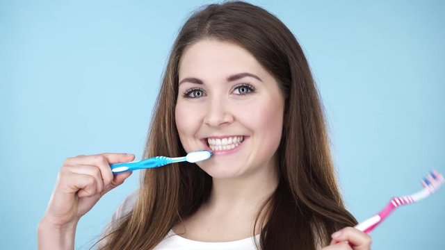 Woman holding two brushes for teeth cleaning. Happy positive smiling girl with toothbrush. Oral daily hygiene. Studio shot on blue background 4K ProRes HQ codec