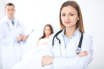Friendly female doctor on the background with patient in the bed and his physician