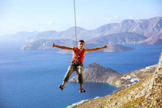 Rock climber swinging on rope and showing thumbs up