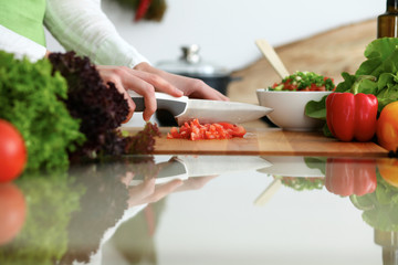 Closeup of human hands cooking vegetables salad in kitchen on the glassr table with reflection. Healthy meal and vegetarian concept