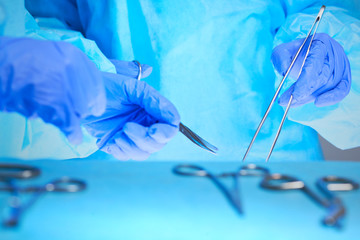 Close-up of of surgeons hands at work in operating theater toned in blue. Medical team performing operation
