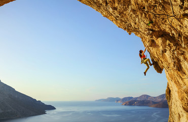 Young woman climbing challenging route in cave at sunset - obrazy, fototapety, plakaty