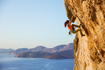 Female rock climber on challenging route on cliff, view of coast below