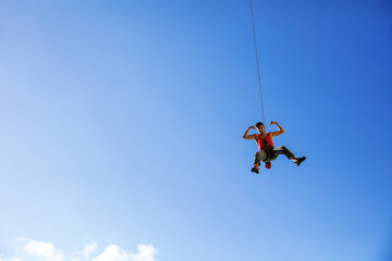 Fototapeta premium Rock climber swinging on rope and flexing muscles