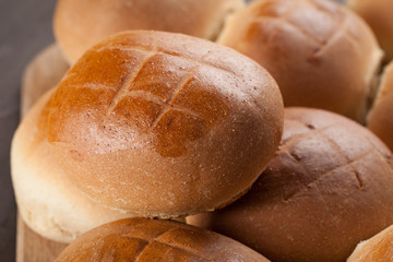 Large Baked Homemade Rolls stacked on cutting board on dark wooden background horizontal shot