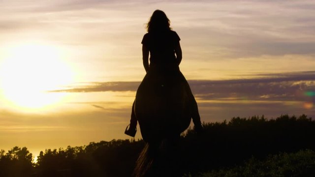 4k UHD Slog3 Cine Long Lens of woman riding English style on a Thoroughbred horse walking away silhouetted with dramatic setting sun over ocean in front of her then turning right SDF8
