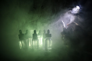 Vape concept. Smoke clouds and vape liquid bottles on dark background. Light effects. Useful as...
