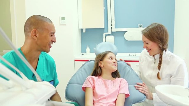 Friendly male dental surgeon and female dentist talking with cute little patient