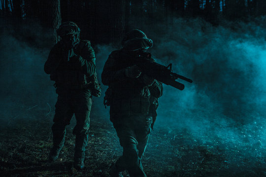 Pair of soldiers in the smoke in action on battle operation. Dark gloomy night, they moving stealthy