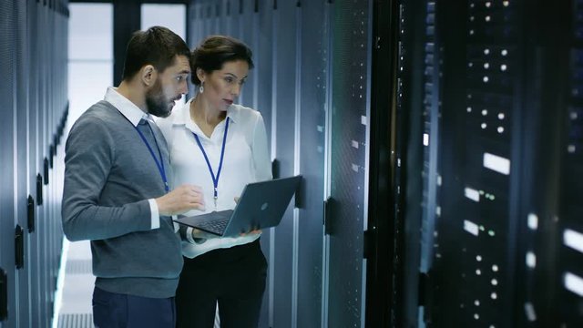 Male IT Specialist Holds Laptop and Discusses Work with Female Server Technician. They're Standing in Data Center, Rack Server Cabinet is Open. Shot on RED EPIC-W 8K Helium Cinema Camera.