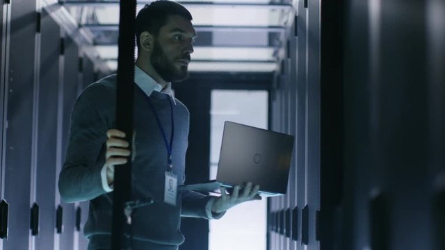 Male IT Engineer Opens Server Cabinet while Holding Laptop. He Works in Big Data Center Shot on RED EPIC-W 8K Helium Cinema Camera.