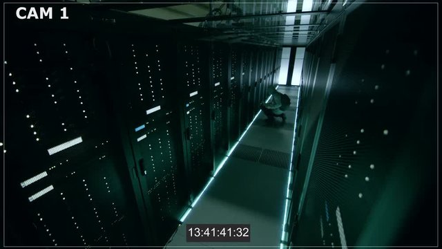 Security Camera N1 Footage of Hacker in a Hoodie Inflitrating Data Center, With His Laptop He Connects to One of The Rack Servers. Shot on RED EPIC-W 8K Helium Cinema Camera.
